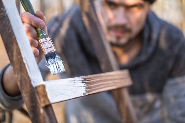 Een man schildert met witte verf op houten planken. Man in industrieel concept. Er is een plek voor tekst, het object is dichtbij