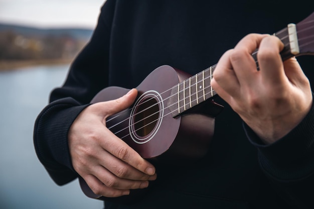 Gratis foto een man speelt de ukelele-gitaar in de natuur close-up van zijn hand