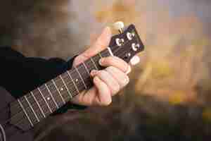 Gratis foto een man speelt de ukelele-gitaar in de natuur close-up vingers klemmen de snaren vast