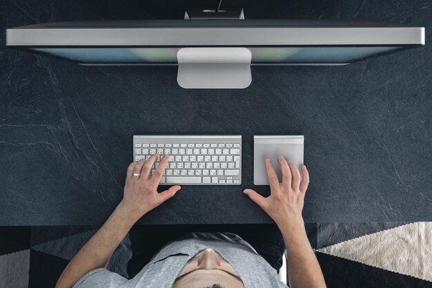 Een man werkt op een computer bovenaanzicht desktopcomputer op een tafel