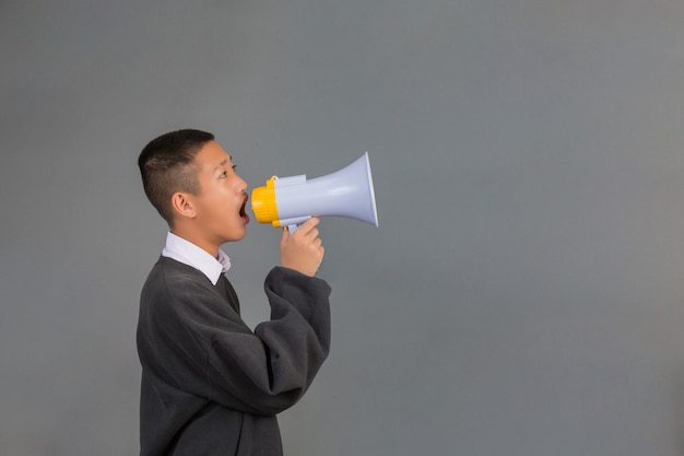 Een mannelijke Aziatische student draagt een zwarte trui met behulp van een megafoon en staat op een grijs.