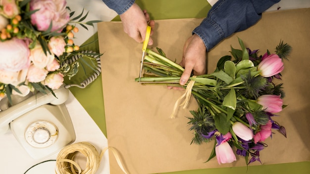 Een mannelijke bloemist die de stam van bloemenboeket snoeit in de bloemwinkel