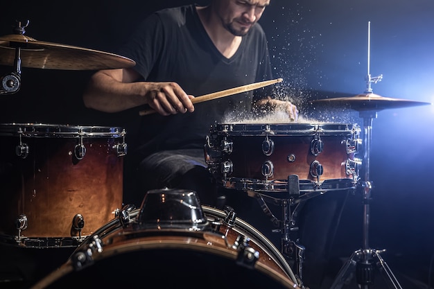 Een mannelijke drummer speelt drumstokken op een snaredrum met opspattend water in een donkere kamer.