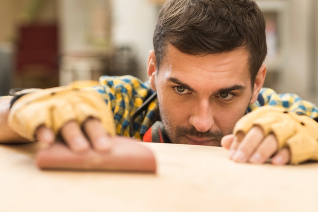 Gratis foto een mannelijke timmerman die schuurpapier op houten oppervlakte gebruikt