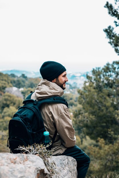 Een mannelijke wandelaarzitting op rots met zijn rugzak die mening bekijkt