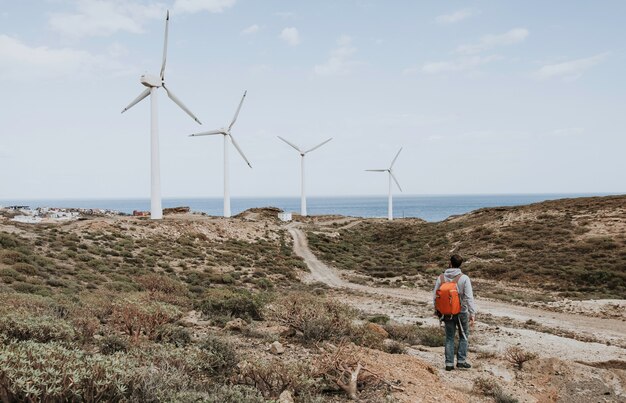 Een mannetje met een rode rugzak staan en kijken naar de windmolens