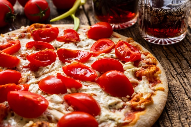 Een Margarita-pizza met kaas en tomaten op een houten bord in de buurt van een paar glazen met drankjes