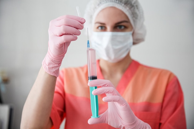 Een medische werker in een roze gewaad, een witte pet en roze handschoenen houdt een spuit met een vaccin vast
