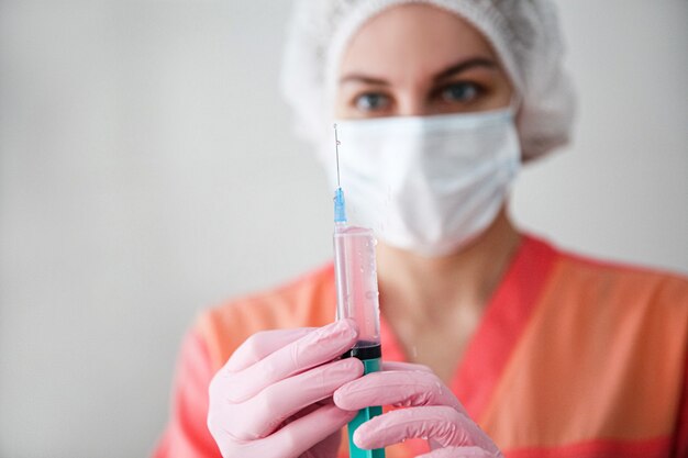 Een medische werker in een roze gewaad, een witte pet en roze handschoenen houdt een spuit met een vaccin vast