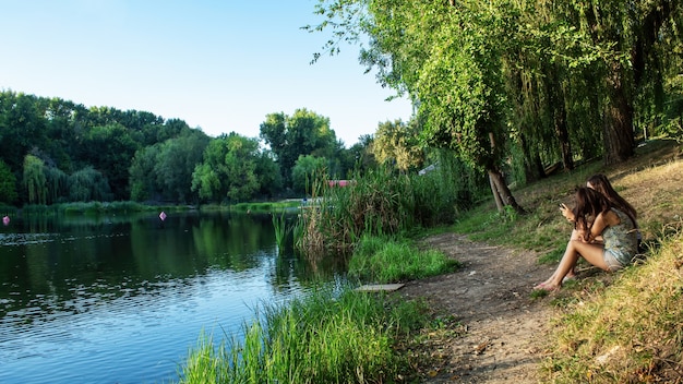 Een meer met veel groene bomen weerspiegeld in het water, twee meisjes zitten op de kust en riet erlangs in Chisinau, Moldavië