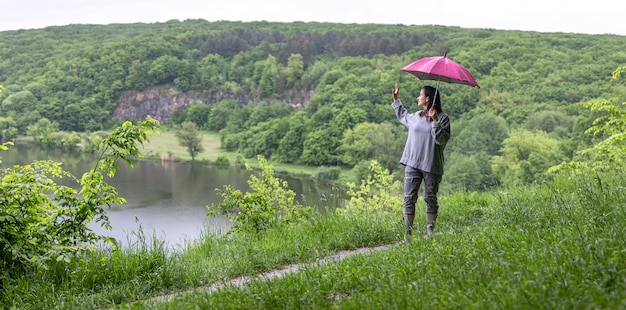 Een meisje op een wandeling in het bos onder een paraplu tussen de bergen bij het meer.