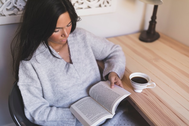 Gratis foto een meisjeszitting op stoellezingsboek met koffiekop op lijst