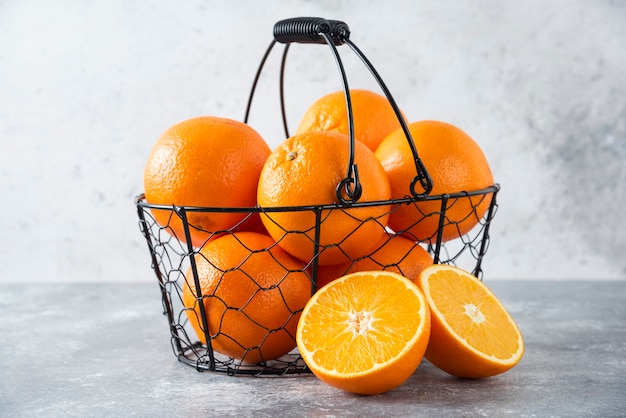 Een metallic zwarte mand vol sappig oranje fruit op stenen tafel.