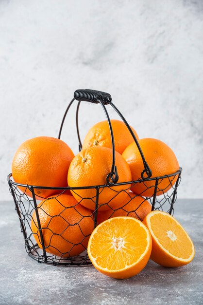 Een metallic zwarte mand vol sappig oranje fruit op stenen tafel.