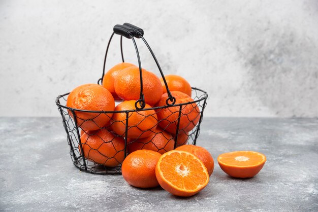 Een metallic zwarte mand vol sappig oranje fruit op stenen tafel.