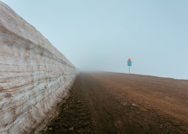 Een mistige modderige weg naast een muur en verkeersborden