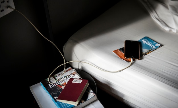 Een mobiele telefoon opladen liggend op het bed met een bangkok, thailand reisgids en brochure