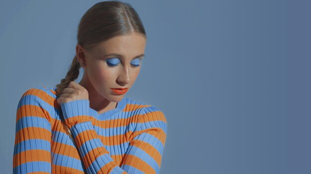 Een mooi jong model poseert en kijkt naar beneden met oogmake-up in blauwe tinten
