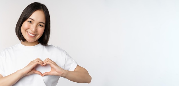 Een mooie aziatische vrouw die lacht en een hartteken toont, drukt tederheid en genegenheid uit over een witte b