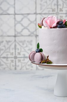 Een mooie en delicate taart voor een meisje. het dessert is versierd met verse bosbessen, rozen en macaronscakes.