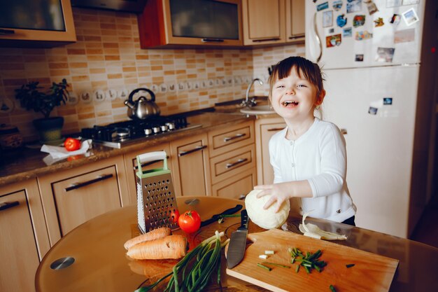 Een mooie jonge kleine dochter kookt thuis in de keuken