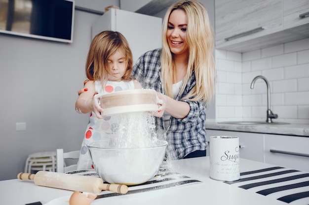 Een mooie jonge moeder met haar kleine dochter kookt thuis in de keuken