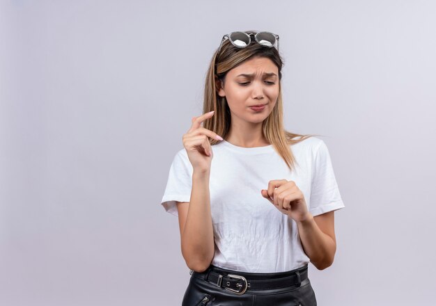 Een mooie jonge vrouw in wit t-shirt met zonnebril die zich iets op een witte muur probeert te herinneren