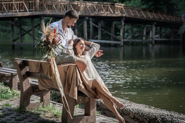Een mooie jonge vrouw met bloemen en haar man zitten op een bankje en genieten van communicatie, een date in de natuur, romantiek in het huwelijk.