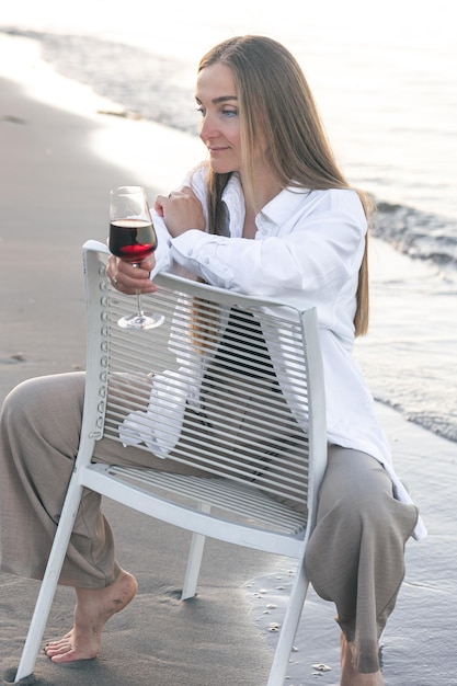 Een mooie vrouw met een glas wijn aan de kust zit op een stoel