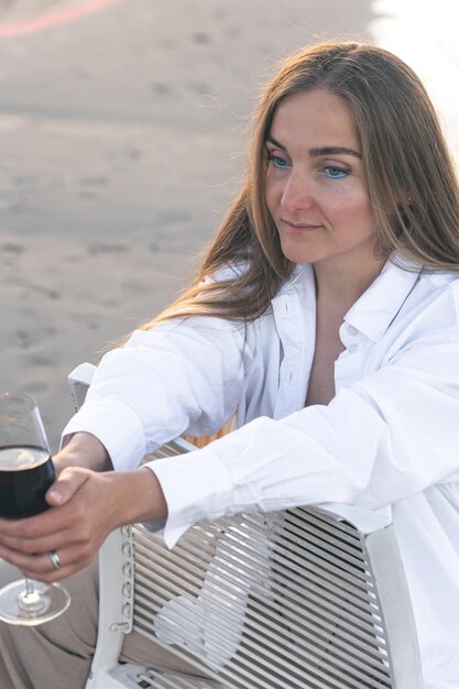 Een mooie vrouw met een glas wijn aan de kust zit op een stoel