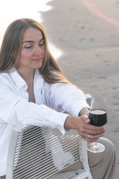 Een mooie vrouw met een glas wijn aan de kust zit op een stoel