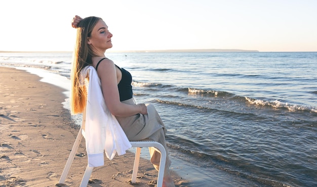 Een mooie vrouw zit op een stoel in de buurt van de zee