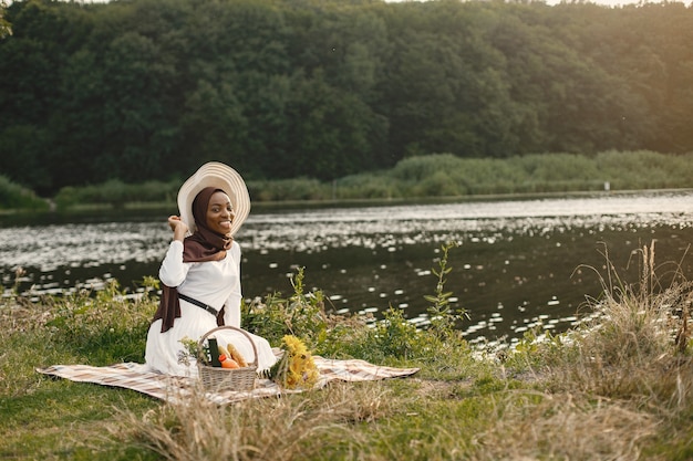 Gratis foto een moslimvrouw zit op de geruite picknickdeken bij de rivier