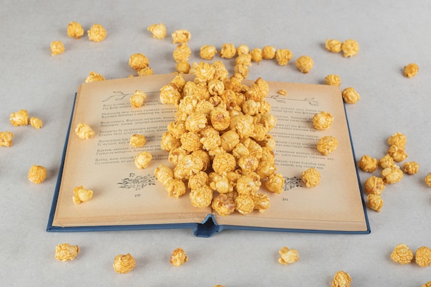 Een opengeslagen boek met een hoop met karamel bedekte popcorn overal verspreid op marmer.