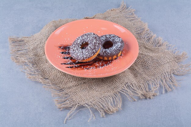 Een oranje plaat van heerlijke chocolade donuts met hagelslag op een zak.