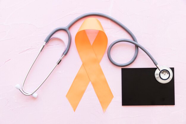 Een oranje voorlichtingslinten met stethoscoop over lei op roze achtergrond