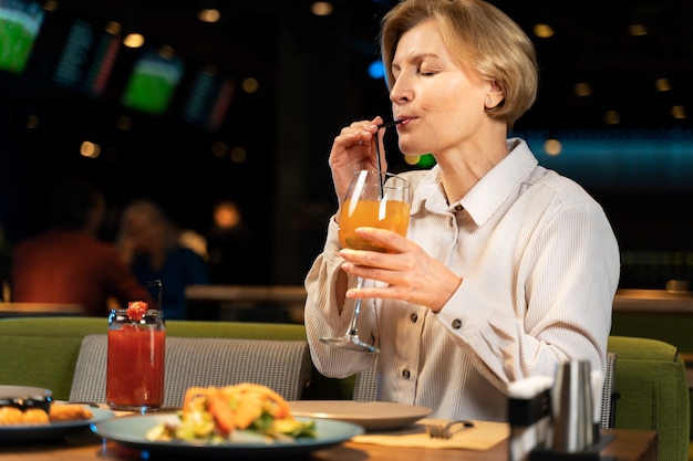 Een oudere vrouw drinkt in een restaurant.