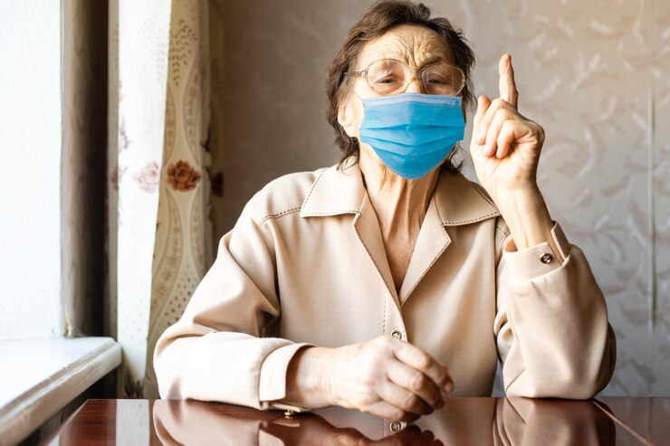 Gratis Foto een oudere vrouw met een masker bij het raam.