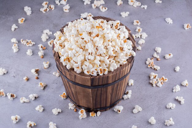 Een overdreven gevulde houten emmer in het midden van verspreide popcorn op marmeren achtergrond. Hoge kwaliteit foto