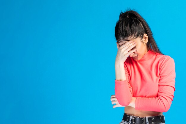 Een overstuur jongedame legde haar hand op haar voorhoofd en keek neer op een blauwe achtergrond