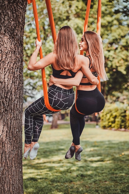 Een paar beste vrienden chillen op de oranje stroppen onder de boom in het zomerpark.