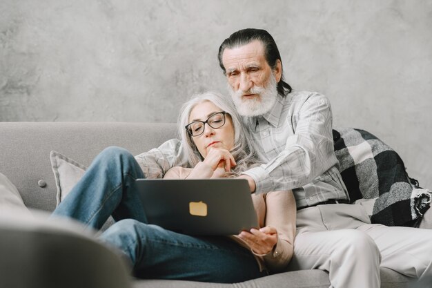 Een paar senioren glimlachen en kijken naar dezelfde laptop die omhelsd is op de bank, lockdown en quarantaine levensstijl