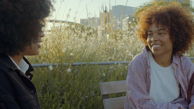 Een paar zwarte vrouwen van gemengd ras praten in het park omringd door bloemen in de ochtendzon Filmkleuren soft focus