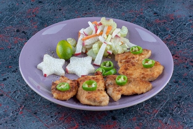 Een paars bord kipnuggets met chilipeper.