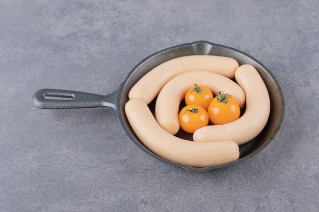 Een pan met gekookte worstjes en gele tomaten.