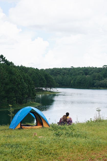 Een panfoto van een paar knuffelen op de rivier bij de tent met hun rug naar de camera