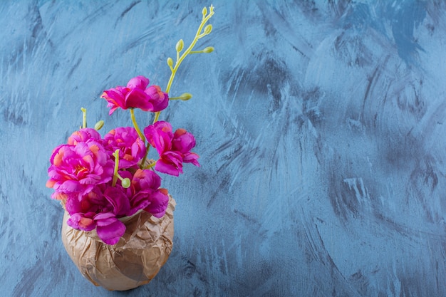 Een papieren vaas met mooie frisse paarse bloemen op blauw.