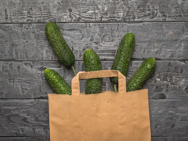 Een papieren zak met gemorste komkommers op een houten tafel. verse groenten in milieuvriendelijke verpakking.