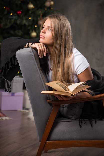 Een peinzende jonge vrouw in zwarte deken zittend met een boek