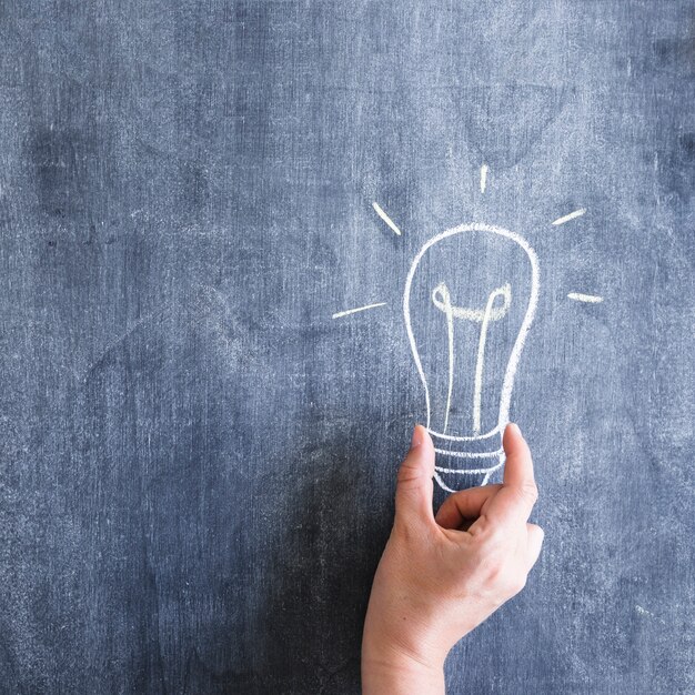 Een persoon die een gloeilamp vasthoudt die op een krijtbord is getekend